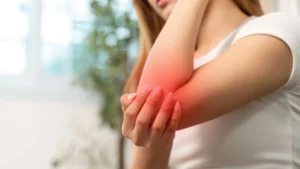 Persona sujetándose el codo con gesto de dolor, con enrojecimiento visible en la zona, representando una epicondilitis o codo de tenista.